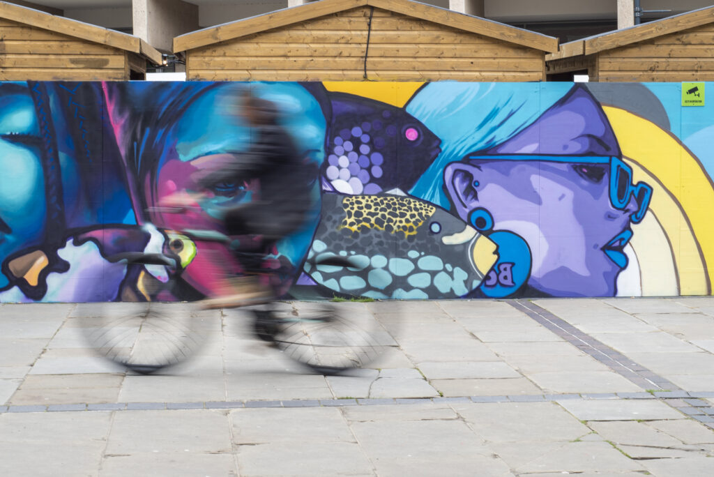 A person cycling fast in front of a graffiti wall.